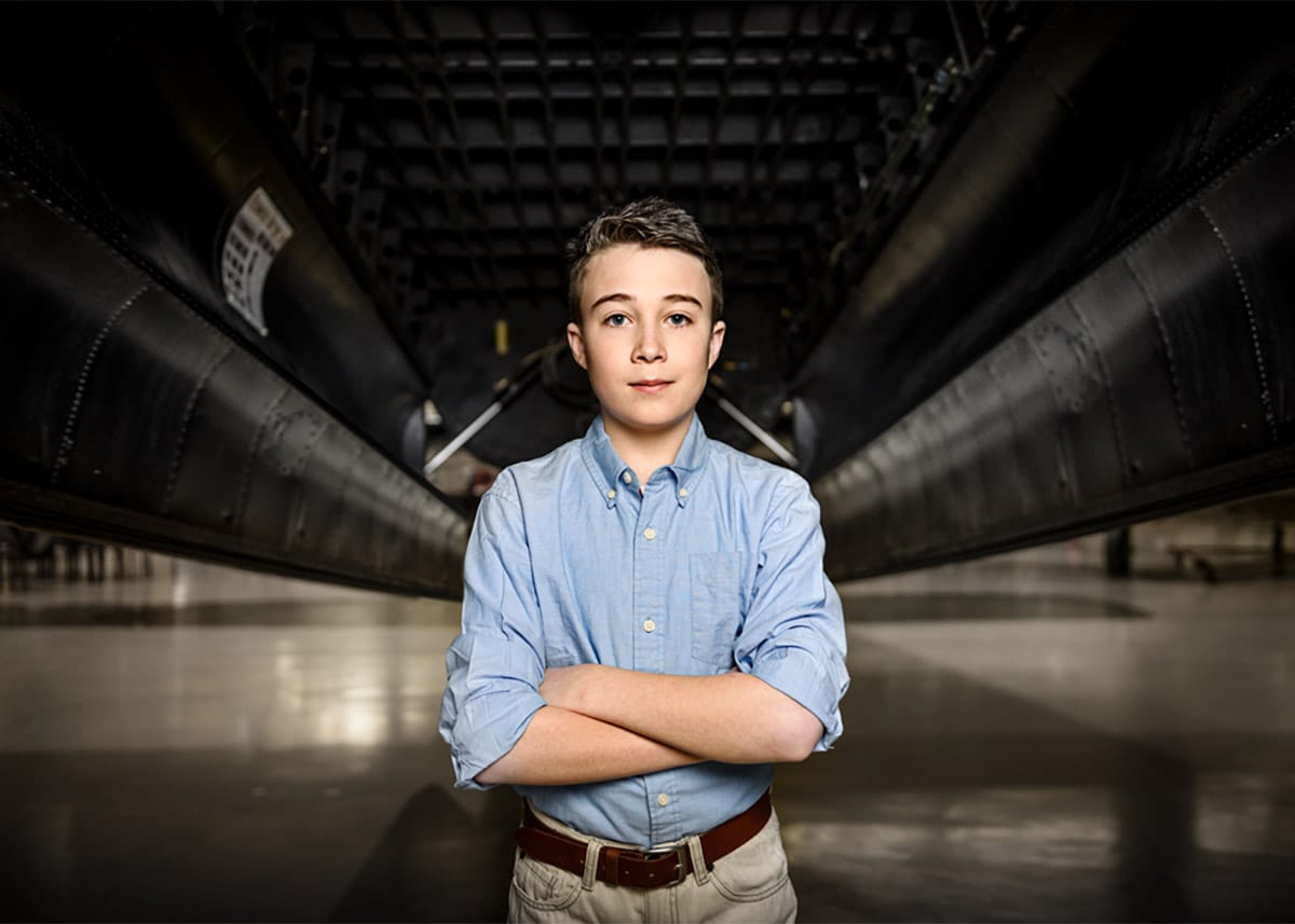 A portrait photograph of a young boy posing formally with his arms crossed